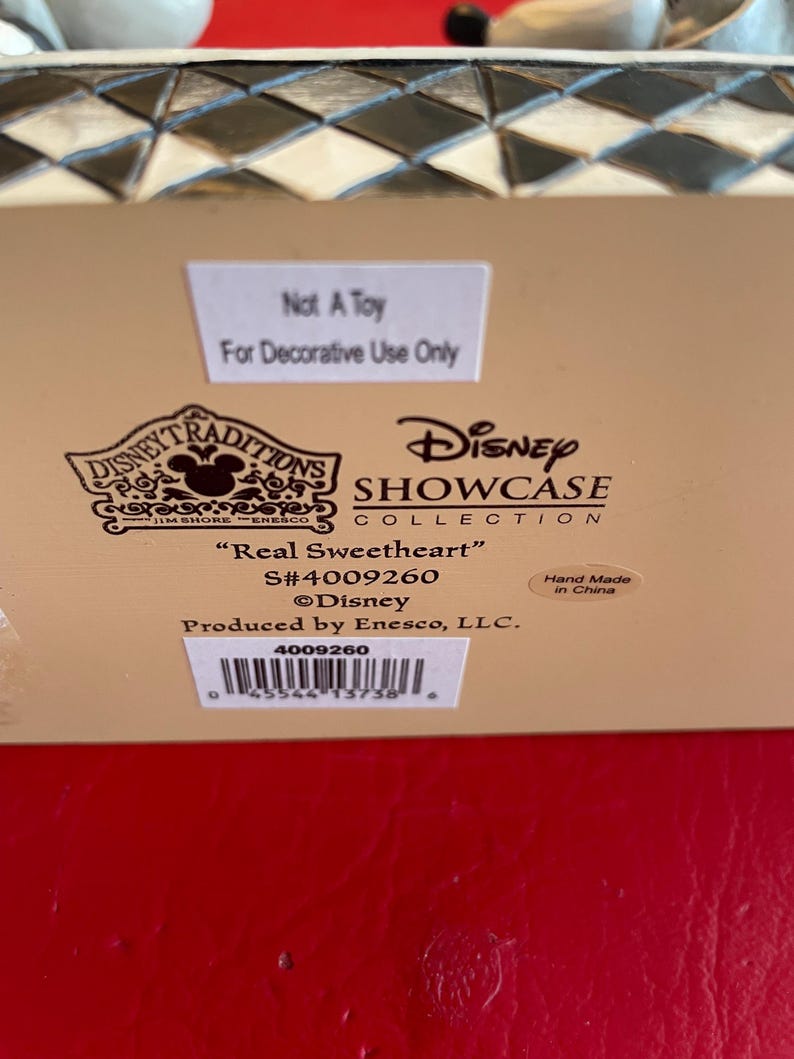 Pu&ograve; includere: Una statuetta in ceramica bianca di Topolino e Minnie Mouse vestiti con i loro iconici abiti rosso e nero. La statuetta fa parte della collezione Disney Traditions Showcase e si intitola "Real Sweetheart". La statuetta &egrave; realizzata a mano in Cina e ha il numero di prodotto 4009260.