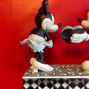 Pu&ograve; includere: Una statuetta in bianco e nero di Topolino e Minnie Mouse che tiene un cuore. La statuetta &egrave; su una base piastrellata in bianco e nero.