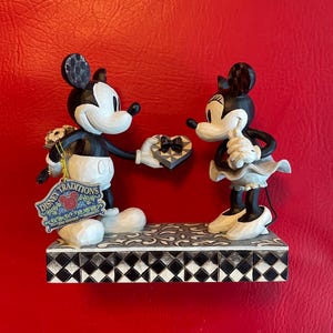 Pu&ograve; includere: Figurina in bianco e nero di Topolino che presenta una scatola di cioccolatini a forma di cuore a Topolina. La figurina &egrave; su una base a scacchi bianco e nero con un'etichetta Disney Traditions.