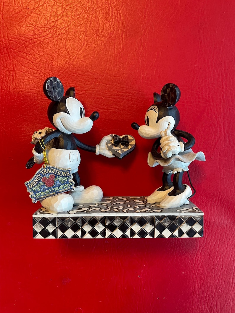 Pu&ograve; includere: Figurina in bianco e nero di Topolino che presenta una scatola di cioccolatini a forma di cuore a Topolina. La figurina &egrave; su una base a scacchi bianco e nero con un'etichetta Disney Traditions.
