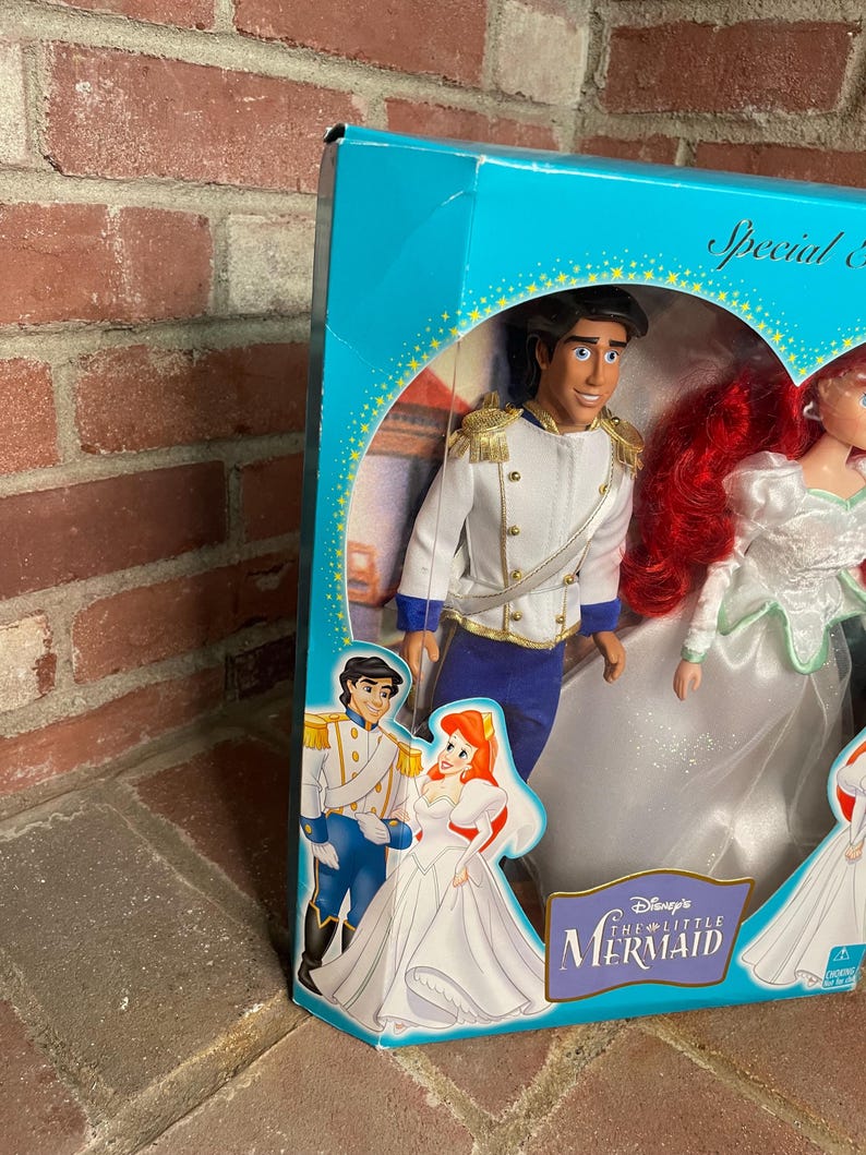 May include: A boxed set of Disney's The Little Mermaid dolls. The dolls are Prince Eric and Ariel in wedding attire. The box is teal with gold accents and features illustrations of the characters. The box reads "Special Edition".