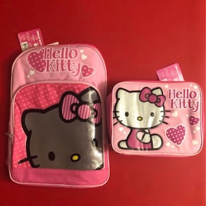 May include: Pink Hello Kitty backpack and lunch bag set. The backpack has a large Hello Kitty face with a pink bow and a pink polka dot pattern. The lunch bag has a smaller Hello Kitty face with a pink bow and a pink heart pattern.