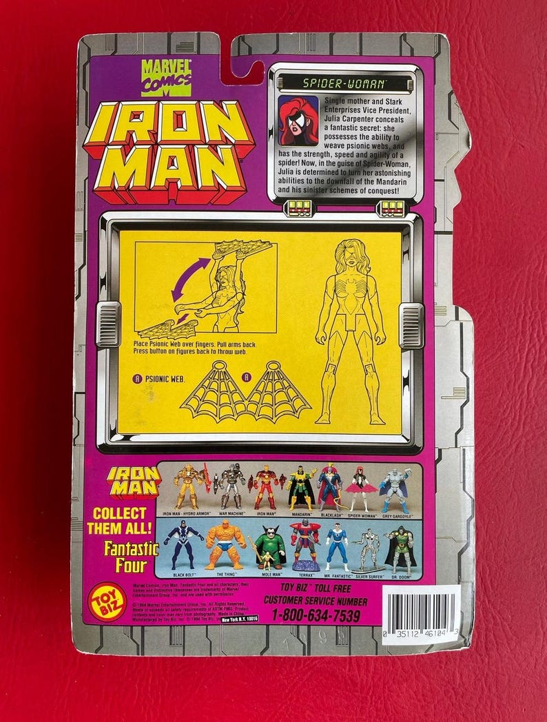 May include: A Spider-Woman action figure from the Marvel Comics Iron Man series. The figure is posed with her arms outstretched, holding a web. The figure is wearing a red and black costume with a spider symbol on her chest. The packaging features a yellow background with the Marvel Comics logo and the words "Iron Man" in large, bold letters. The back of the packaging includes a description of the character and instructions on how to play with the figure.