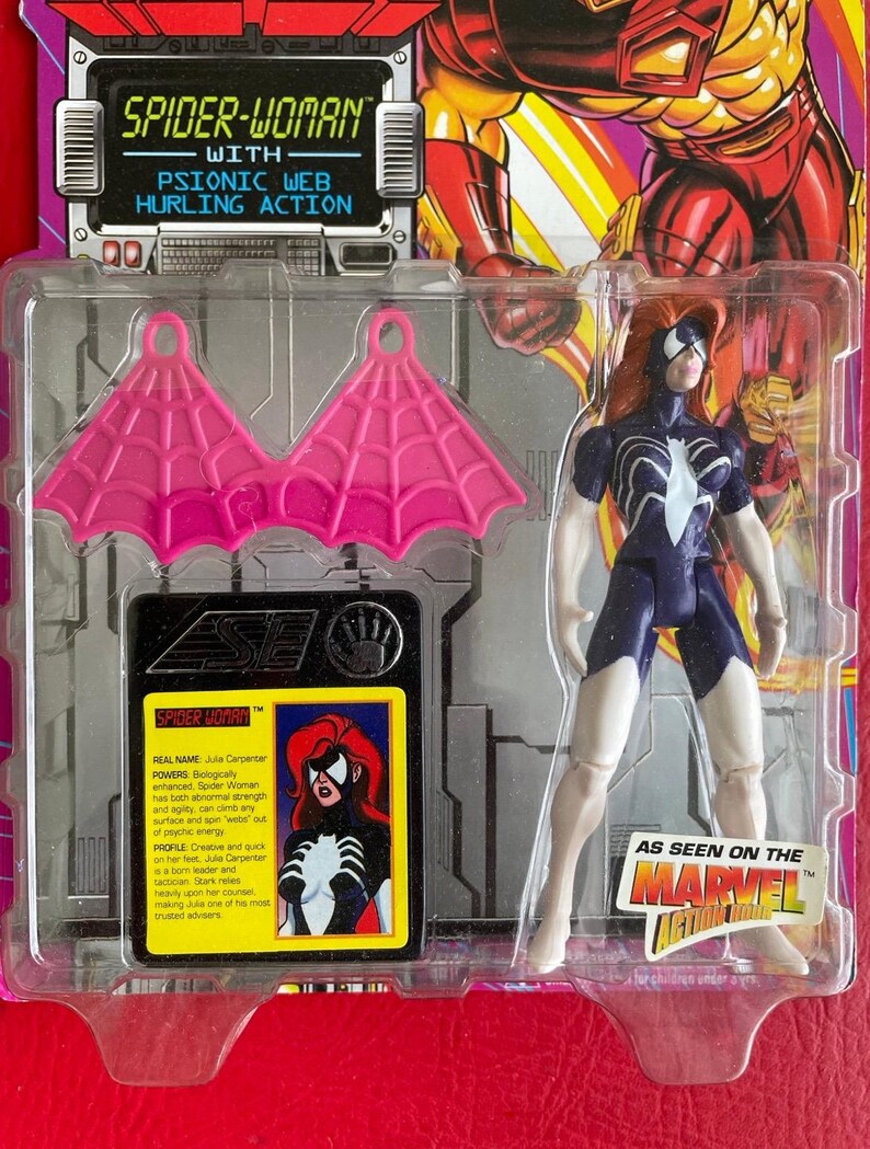 May include: A Spider-Woman action figure with pink web wings, a blue and white suit, and red hair. The figure is packaged in a plastic blister pack with a card featuring a comic book style illustration of Spider-Woman. The card includes the text "SPIDER-WOMAN", "WITH PSIONIC WEB HURLING ACTION", "REAL NAME: Julia Carpenter", "POWERS: Biologically enhanced. Spider-Woman has both abnormal strength and agility, can climb any surface and spin 'webs' out of psychic energy", "PROFILE: Creative and quick on her boot Julia Carpenter is a born leader and tactician. Stark relies heavily upon her counsel, making Julia one of his most trusted advisers."