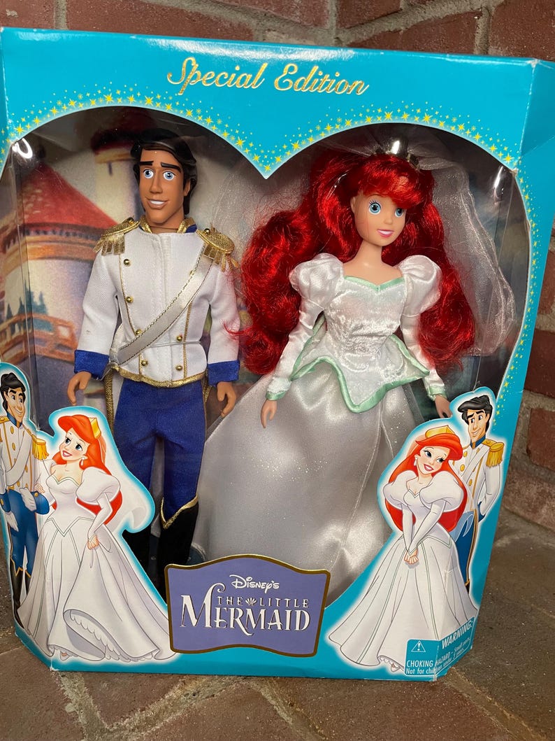 May include: A Special Edition Little Mermaid doll set featuring Ariel in a white wedding dress and Prince Eric in a white and blue uniform. The dolls are in a heart-shaped window box with the movie logo and illustrations.