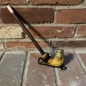 May include: A vintage wooden pipe with a yellow ceramic bowl and a brass lid. The pipe has a long, thin stem and a small, round bowl. The bowl is decorated with a floral design. The pipe is in good condition and has a patina of age.