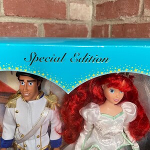 May include: A Special Edition box set featuring two dolls: Prince Eric in a white jacket with gold accents and blue pants, and Ariel in a white dress with red hair. The box has a blue top with the words "Special Edition".
