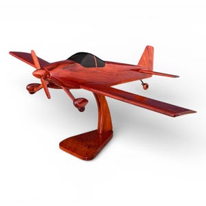 May include: A wooden model airplane with a dark cherry finish. The propeller, wings, and tail are visible. The plane is mounted on a matching wooden stand. The cockpit is black.