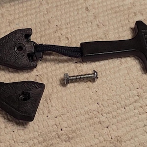 May include: Black replacement latch kit for a cooler, including a handle with "YETI" text, a latch, and a small piece. A screw is also included. The parts are made of black plastic and are designed to replace a broken cooler latch.