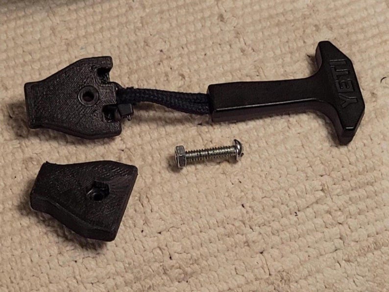May include: Black replacement latch kit for a cooler, including a handle with "YETI" text, a latch, and a small piece. A screw is also included. The parts are made of black plastic and are designed to replace a broken cooler latch.