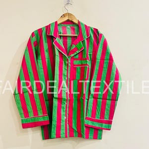 May include: A set of pajamas with vertical stripes in bright pink and green. The long-sleeved top has a chest pocket and white trim along the collar, cuffs, and pocket. The pajamas are hanging on a wooden hanger.