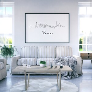 May include: A black framed print of a line drawing of the Rome skyline with the word "Rome" written below the skyline. The print is hanging on a white wall above a striped couch in a living room.
