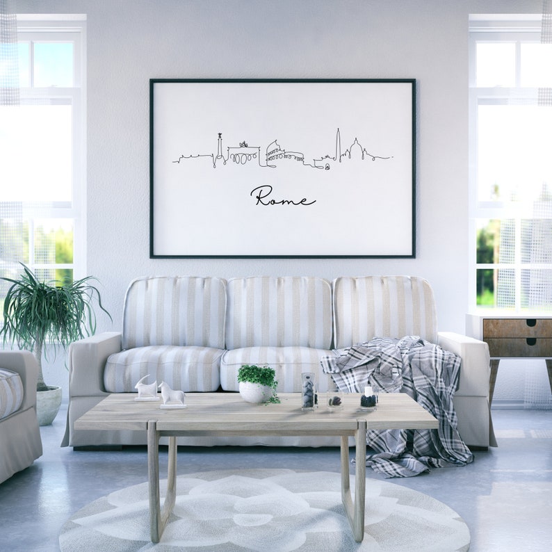 May include: A black framed print of a line drawing of the Rome skyline with the word "Rome" written below the skyline. The print is hanging on a white wall above a striped couch in a living room.