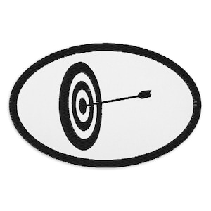 Puede incluir: Parche bordado en blanco y negro con un blanco y una flecha en el centro. El blanco tiene círculos concéntricos y la flecha apunta al centro.