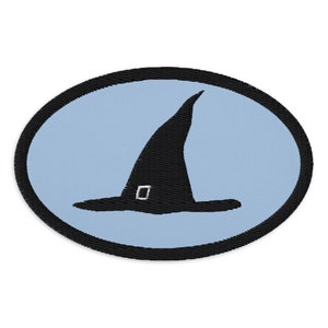 Pode incluir: Patch bordado com um chapéu de bruxa preto com fivela, sobre um fundo oval azul claro. O chapéu tem uma coroa pontiaguda e uma aba larga. O patch é delineado com uma borda preta.
