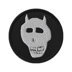 May include: A black embroidered patch with a white skull with horns. The skull has a toothy grin.