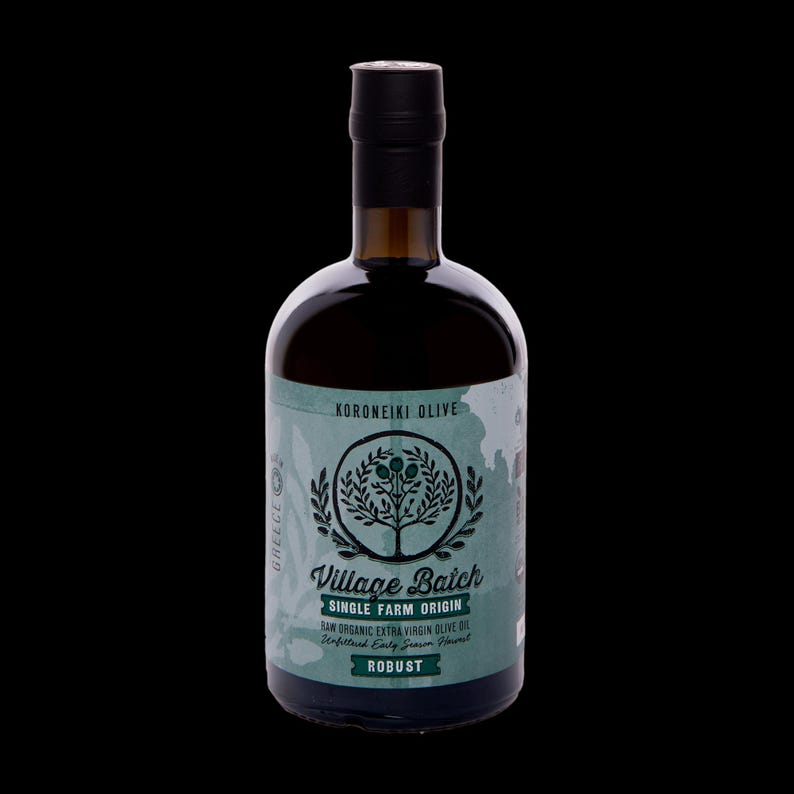 May include: A dark glass bottle of Village Batch single farm origin raw organic extra virgin olive oil. The label is light green with a dark green tree illustration, the text Koroneiki Olive, and the word Robust in a dark green rectangular box.
