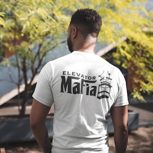 May include: White t-shirt with a black graphic print of a lift with the text "Elevator Mafia" on the back.