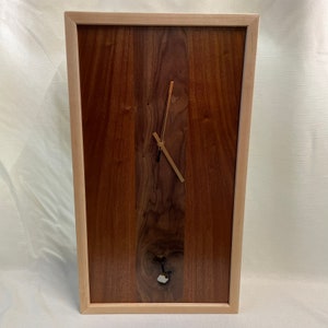 May include: A wooden wall clock with a light wood frame and a dark wood face. The clock has gold hands and a small, light-colored knot in the wood.