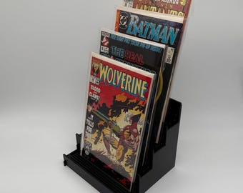 Könnte beinhalten: Schwarzer Comic-Buch-Display-Ständer mit mehreren Comics. Die Comics enthalten Titel wie "Wolverine", "Batman" und "Extinction Agenda". Der Ständer besteht aus schwarzem Kunststoff und hat ein mehrstufiges Design.