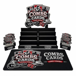 May include: A black display stand with four tiers for trading cards, featuring a large header sign and two smaller side signs. Each sign displays the text COMBS CARDS LUKE COMBS with graphics of a guitar, dice, and a hat. A matching black rectangular playmat is included.