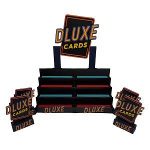 May include: A black card display stand with the text "DLUXE CARDS" in a retro font. The stand has multiple shelves with red and blue accents. Additional "DLUXE CARDS" signs are placed around the display.