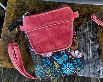 May include: A small pink cork crossbody bag with a floral print and a butterfly design. The bag has a zipper closure and a long adjustable strap.