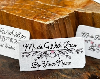 May include: White fabric label with black text and a floral design. The text reads "Made With Love By Your Name".