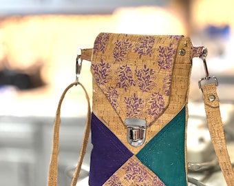 May include: A cork crossbody bag with a flap closure and adjustable strap. The bag features a geometric design with purple and teal accents. The flap is decorated with a purple floral pattern. The bag has a silver-colored clasp.