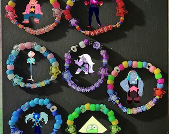 May include: A collection of colorful beaded bracelets featuring cartoon characters and names. Each bracelet has a different color scheme and includes star-shaped and flower-shaped beads. The names "STEVEN", "GARNET", "PEARL", "AMETHYST", "BISUMUTH", and "PERIDOT" are spelled out.