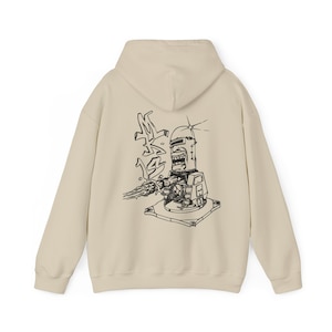 May include: Beige hoodie featuring a black and white illustration of a robot with a weapon and Japanese text. The design is on the back of the hoodie. The hoodie has a hood and long sleeves.