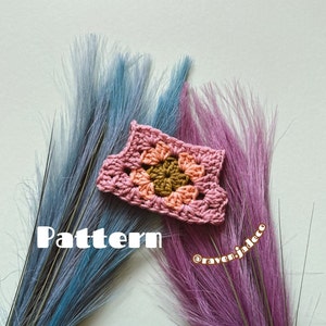 Puede incluir: Un pequeño cuadrado de ganchillo en tonos rosa, melocotón y marrón, con la palabra "Pattern" en texto blanco. El cuadrado se encuentra sobre un fondo de plumas azules y moradas.