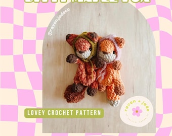 Puede incluir: Dos peluches de zorro de crochet en tonos naranja y marrón. El zorro de la izquierda lleva una chaqueta con capucha verde y el zorro de la derecha lleva una chaqueta con capucha rosa. Los peluches están sentados sobre una superficie de madera. El texto "Bitty Maple Fox" y "Lovey Crochet Pattern" es visible en la imagen.