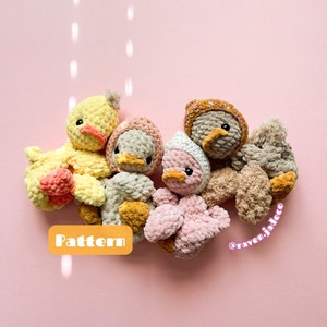 May include: Five crocheted duck plushies in various colors, including yellow, pink, brown, and beige. The plushies are arranged in a circle on a pink background. The text "Pattern" is visible in the lower left corner of the image. The text "@raven.jadeco" is visible in the lower right corner of the image.