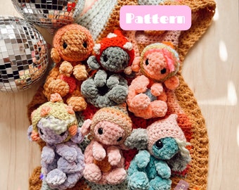 Puede incluir: Una colección de siete juguetes amigurumi de crochet en varios colores, incluyendo rosa, azul, verde y naranja. Los juguetes están sentados sobre una manta de crochet multicolor con la palabra "Pattern" escrita en un rectángulo rosa. La manta está sobre una superficie de madera.