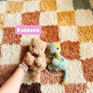 Könnte beinhalten: Zwei gehäkelte Katzenspielzeuge, eines braun und eines blau und gelb, auf einem karierten Teppich. Das Wort "Pattern" ist in rosa auf weißem Hintergrund geschrieben.