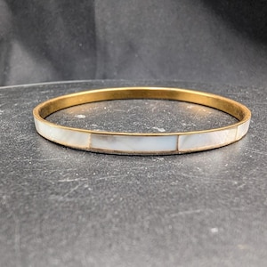 May include: A circular bangle bracelet featuring a thin gold-toned metal frame inlaid with rectangular segments of iridescent white mother-of-pearl. The bracelet has a smooth, polished finish and a consistent width throughout its entire circumference.