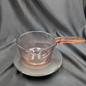 Peut inclure: Une tasse à mesurer en verre translucide violet clair avec une poignée unique et un petit bec verseur. La tasse présente une base circulaire transparente et un bord lisse et arrondi, conçue pour mesurer les liquides en cuisine.