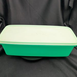 May include: A rectangular, green plastic food storage container with a light green lid. The container has a simple design. The lid fits snugly on top of the container, which is likely for storing food.