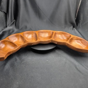 May include: A wooden serving tray with six connected compartments. The tray is curved and has a natural wood grain finish. The compartments are bowl-shaped and appear to be empty. The tray is designed for serving snacks or appetizers.