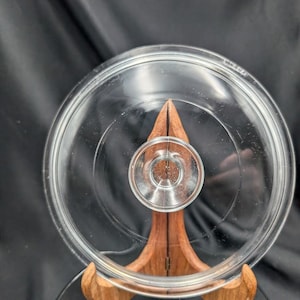 Può includere: Un coperchio in vetro trasparente di forma circolare con una maniglia a pomello centrale rialzata. Il coperchio presenta una superficie liscia e trasparente con un bordo esterno leggermente rialzato e un'area circolare incassata.