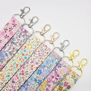 May include: An assortment of floral lanyards with metal swivel clasps. The lanyards display a variety of colours, including pink, blue, purple, and yellow, with diverse floral patterns. The clasps are silver and gold in colour.