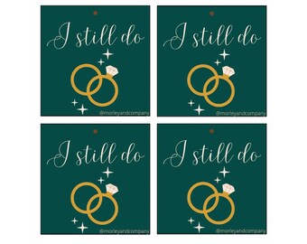 Può includere: Sei etichette regalo stampabili con sfondo verde e anelli dorati con un diamante. Il testo sulle etichette recita "I still do" con l'account social "@morleyandcompany" in fondo a ciascuna etichetta.
