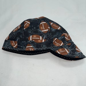 May include: Black and brown welding cap with a pattern of footballs and a football field design.