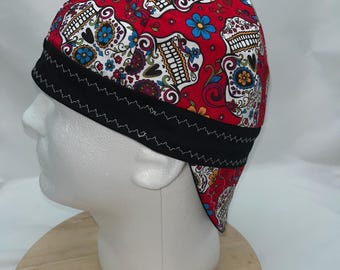 May include: Red welding cap with a black brim and a colorful sugar skull pattern.