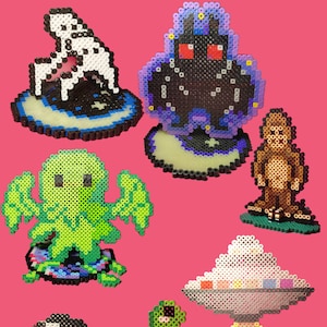 May include: A collection of eight colorful pixel art figures, including a ghost, a monster, a Bigfoot, a Cthulhu, a UFO, a dinosaur, a reaper, and a tent. Each figure is made of small plastic beads and is displayed on a pink background.