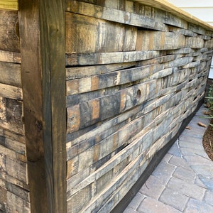 K&ouml;nnte beinhalten: Ein Holztheke aus wiederverwendeten Holzfassdauben. Die Theke ist dunkelbraun gebeizt und hat ein rustikales Aussehen. Die Theke steht vor dem Hintergrund einer Backstein-Terrasse.
