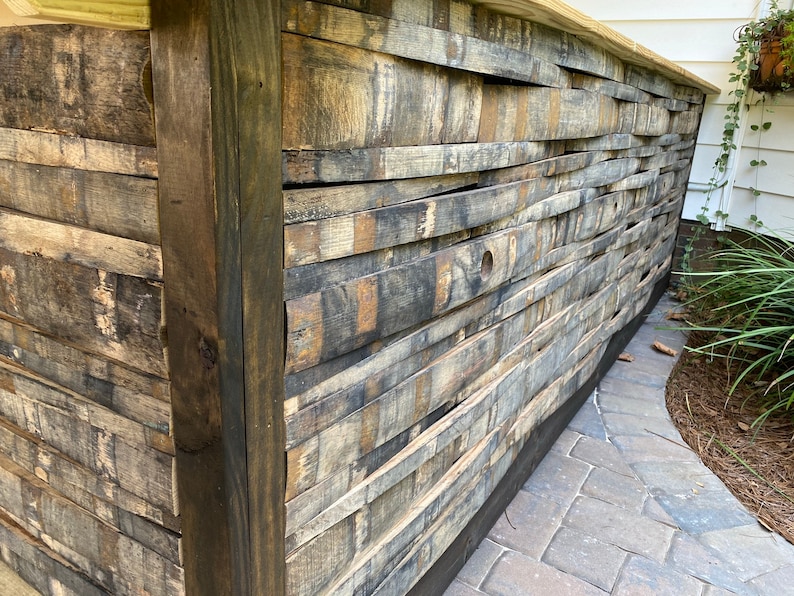 K&ouml;nnte beinhalten: Ein Holztheke aus wiederverwendeten Holzfassdauben. Die Theke ist dunkelbraun gebeizt und hat ein rustikales Aussehen. Die Theke steht vor dem Hintergrund einer Backstein-Terrasse.