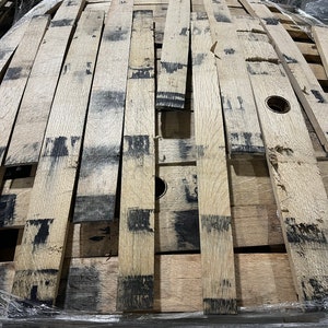 K&ouml;nnte beinhalten: Nahaufnahme eines Stapels aus Holzfassdauben. Die Dauben sind aus hellem braunem Holz und haben eine dunkelbraune F&auml;rbung. Die Dauben sind in einem zuf&auml;lligen Muster angeordnet und &uuml;bereinander gestapelt.
