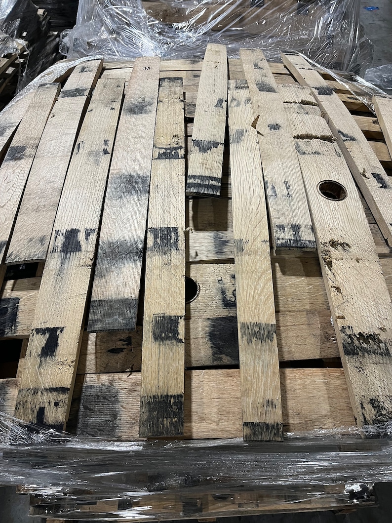 K&ouml;nnte beinhalten: Nahaufnahme eines Stapels aus Holzfassdauben. Die Dauben sind aus hellem braunem Holz und haben eine dunkelbraune F&auml;rbung. Die Dauben sind in einem zuf&auml;lligen Muster angeordnet und &uuml;bereinander gestapelt.
